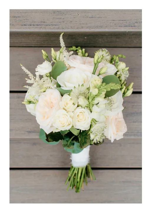 Bouquet of white and pale peach roses with green leaves against wooden background.