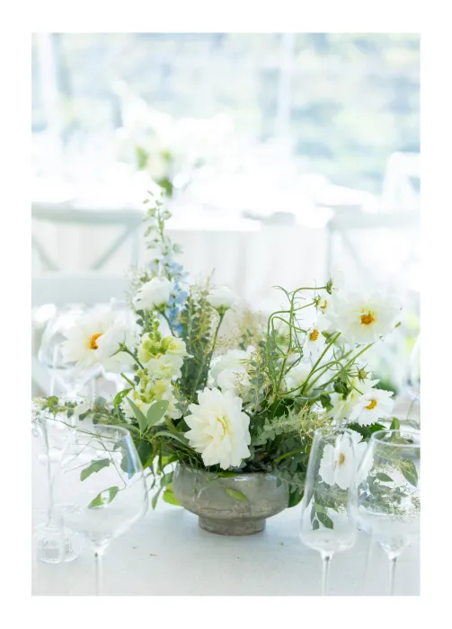 Floral centerpiece with white flowers and greenery on a table with glassware at an event.
