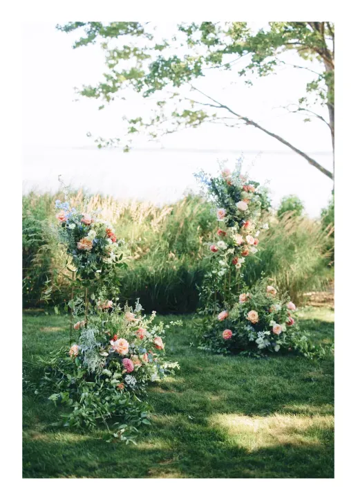 Two lush floral arrangements with pink and white flowers on green stands in a grassy outdoor setting.